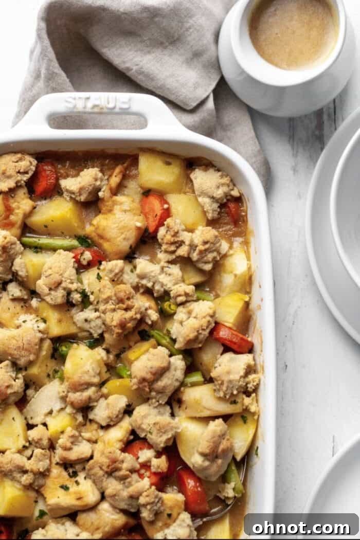 A serving of chicken pot pie casserole with white plates and a small bowl of gravy, ready to be enjoyed.