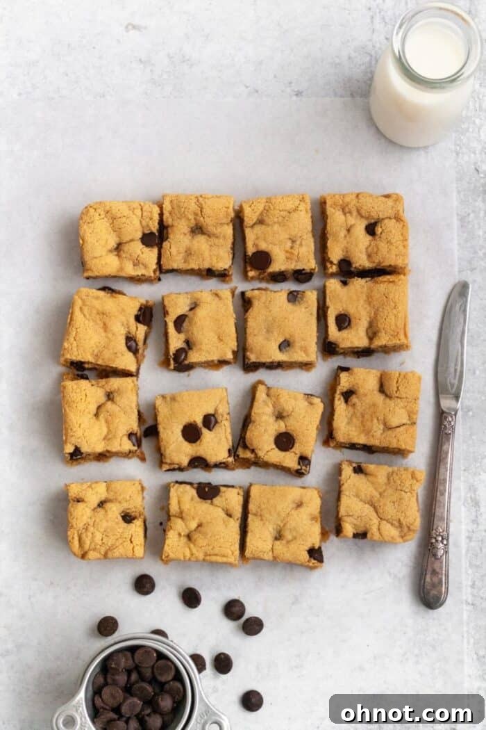 Almond flour blondies on a light colored backdrop with chocolate chips and a glass of milk.