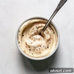 A white bowl with creamy garlic aioli and a silver spoon.