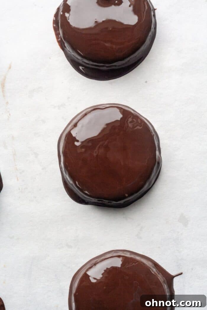 A close-up of a Gluten-Free Thin Mint being dipped into a bowl of smooth, melted mint chocolate coating.