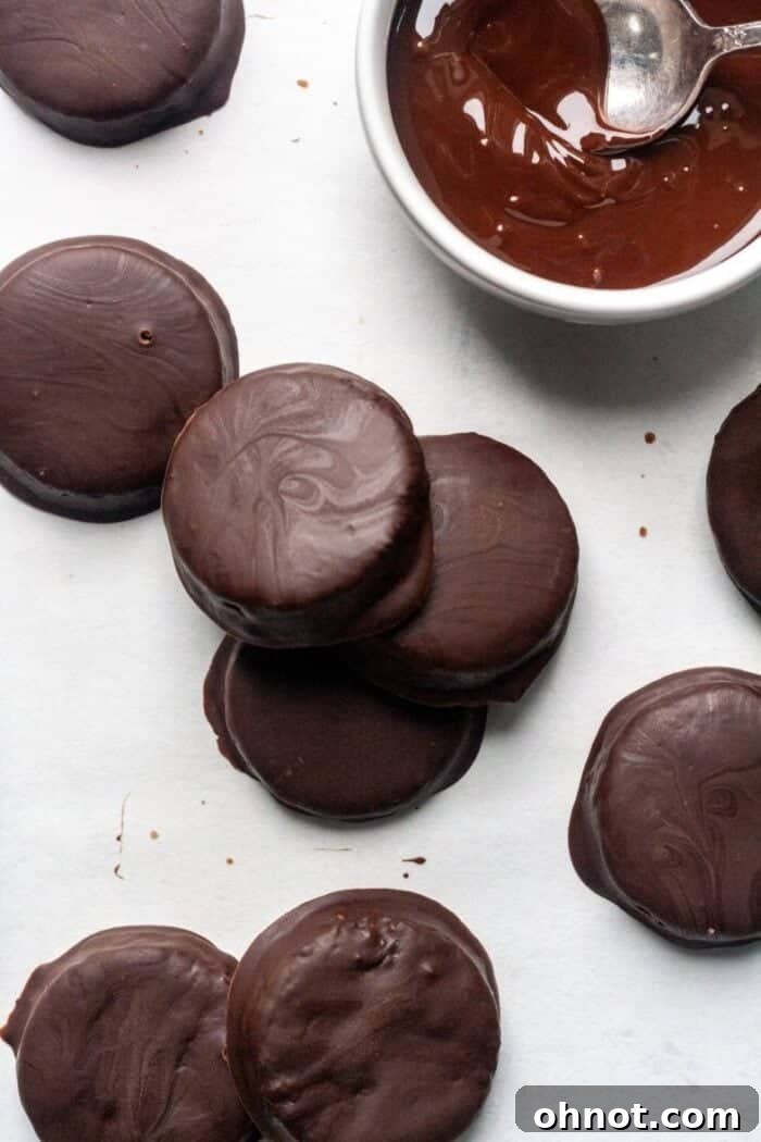Finished Gluten-Free Thin Mint cookies arranged on parchment paper, with a bowl of remaining melted chocolate and a fork nearby.