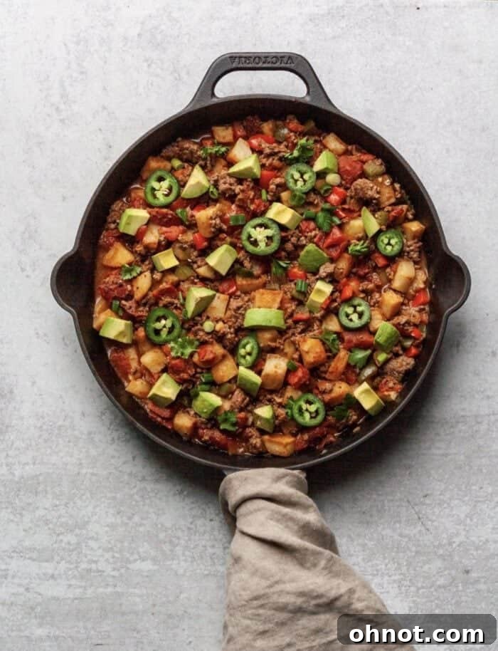 A close-up shot of the Paleo Taco Skillet bubbling in a black cast iron skillet, showcasing the rich texture and vibrant colors of the cooked ingredients.