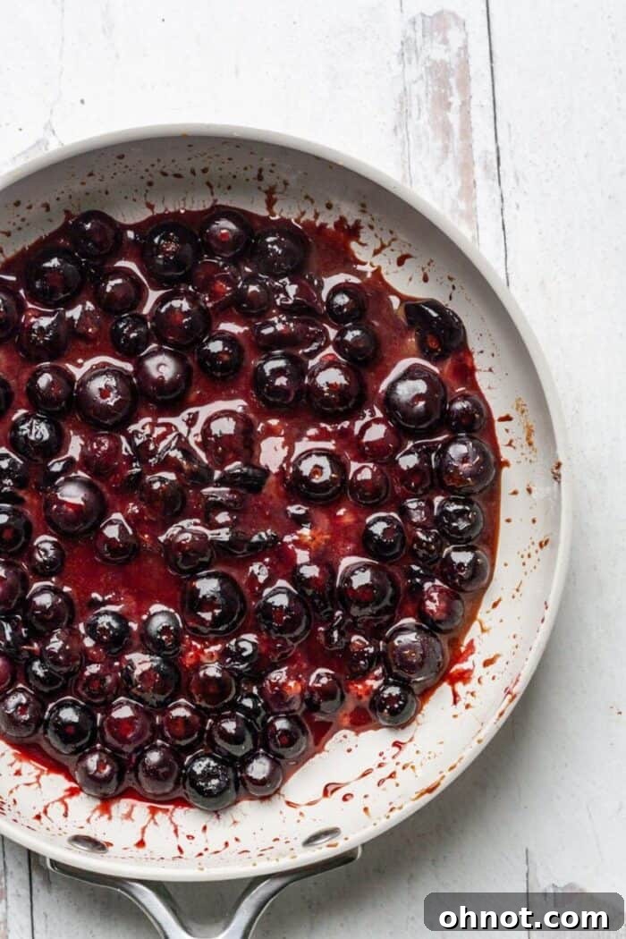 A skillet filled with bubbling Vegan Blueberry Jam, showing the thickening process.