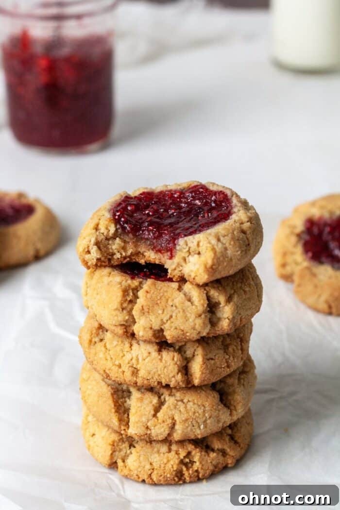 A stack of almond flour thumbprint cookies filled with raspberry jam, showcasing their golden edges and vibrant centers.
