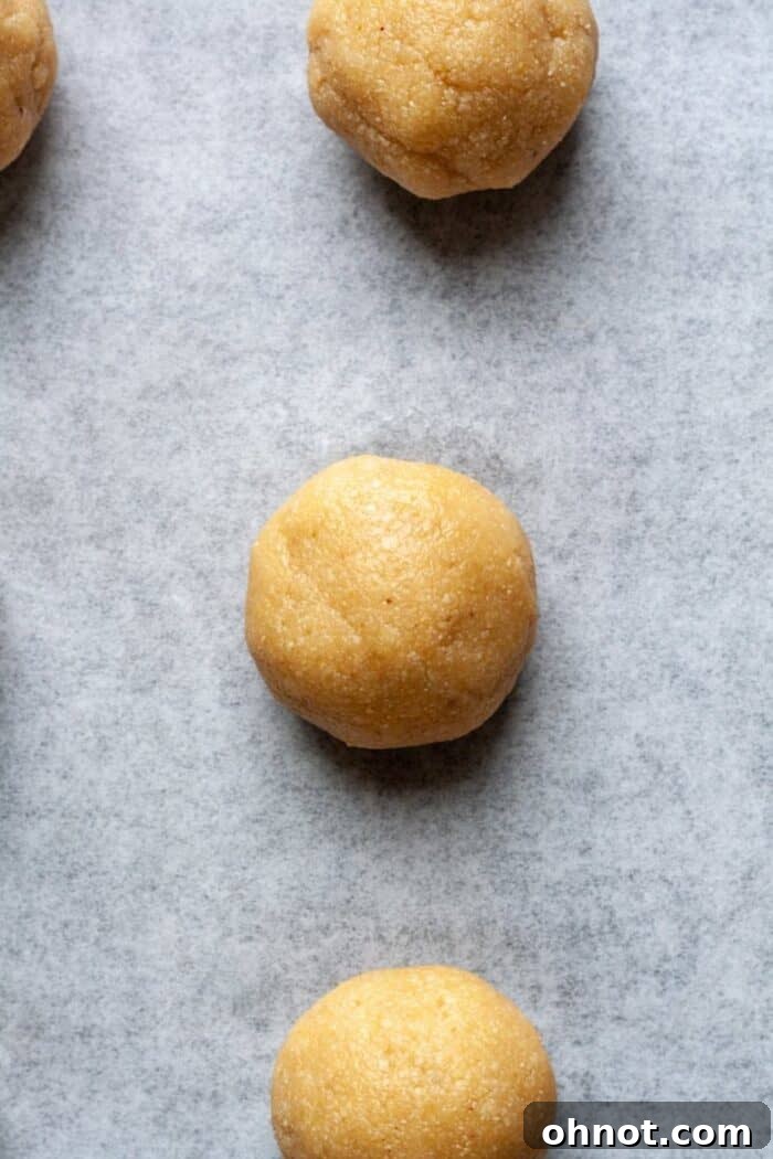 Almond flour thumbprint cookie dough rolled into balls and arranged on parchment paper, ready for the next step.