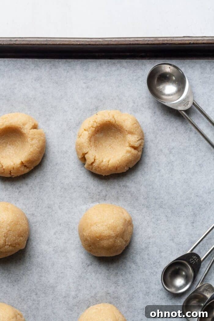 Almond flour thumbprint cookies on a baking sheet, with indentations already made, ready for filling.