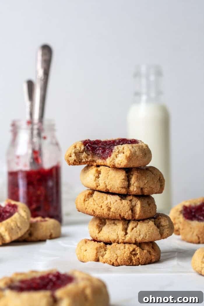 Vegan thumbprint cookies with vibrant raspberry jam, beautifully arranged on a white backdrop, ready to be enjoyed.