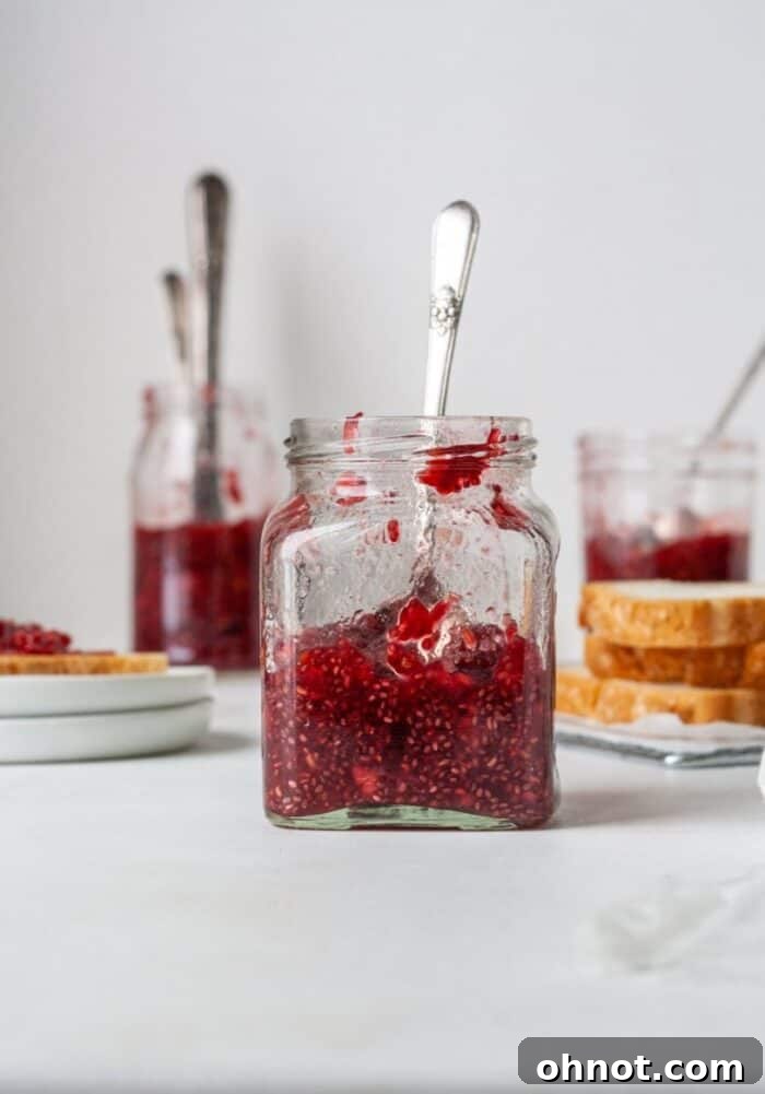 A single clear glass jar, freshly filled with warm, ruby-red sugar-free raspberry chia jelly, steam gently rising, sitting on a countertop ready for cooling.