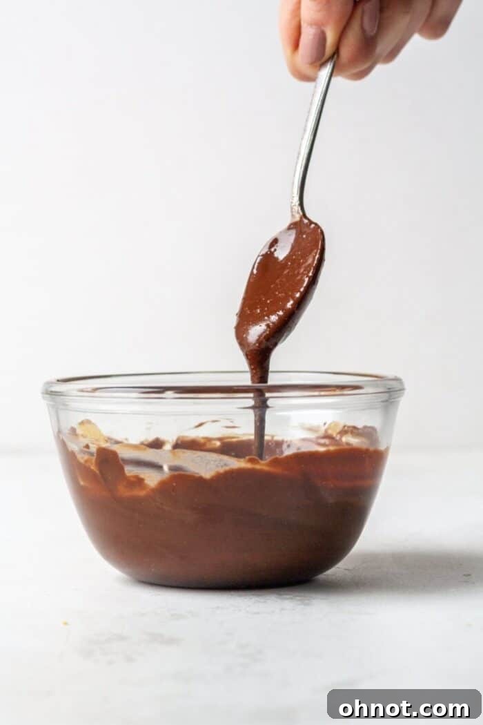 Melted dark chocolate, almond butter, and coconut oil in a clear glass bowl, smooth and glossy.