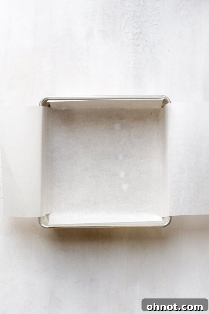 A square baking pan lined with parchment paper, ready for batter.