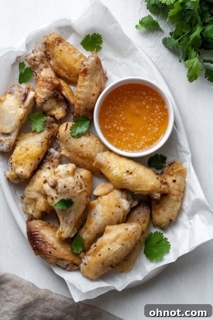 A large white platter generously filled with crispy air-fried chicken wings, garnished with fresh herbs.