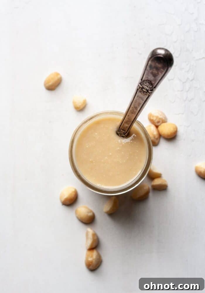 A mason jar filled with freshly made, creamy macadamia nut butter on a wooden surface.
