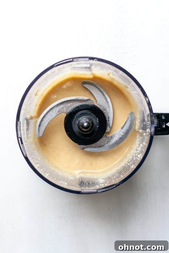 A close-up view of freshly made, ultra-smooth macadamia nut butter swirling in a food processor.