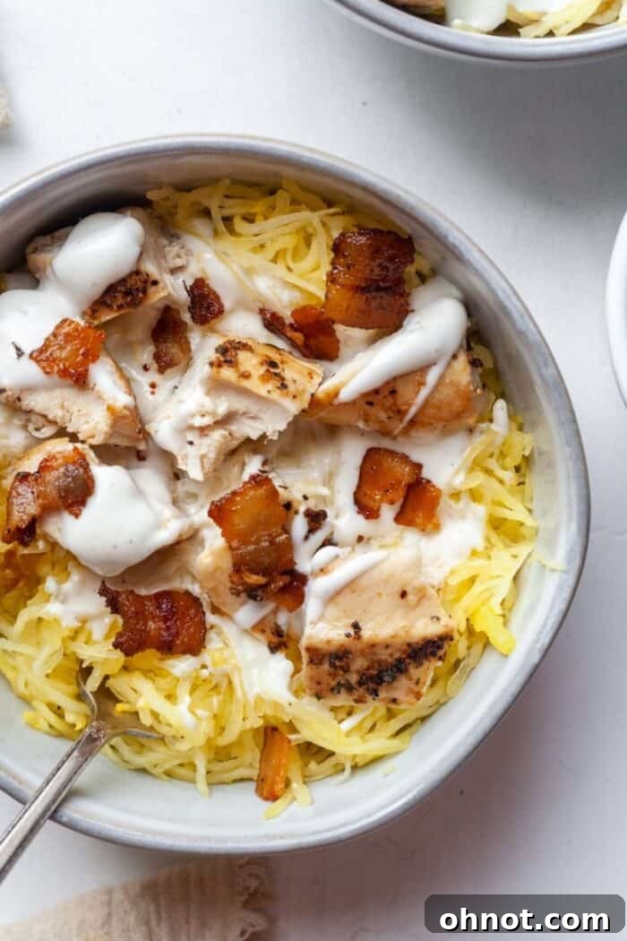 Close-up of a serving bowl filled with Paleo Chicken Bacon Ranch Spaghetti Squash, featuring visible strands of squash, chicken pieces, and bacon, drizzled with Ranch.