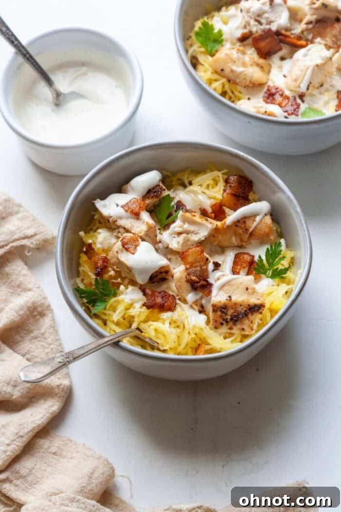 Two white bowls filled with Paleo Chicken Bacon Ranch Spaghetti Squash, ready to be served, on a light surface.