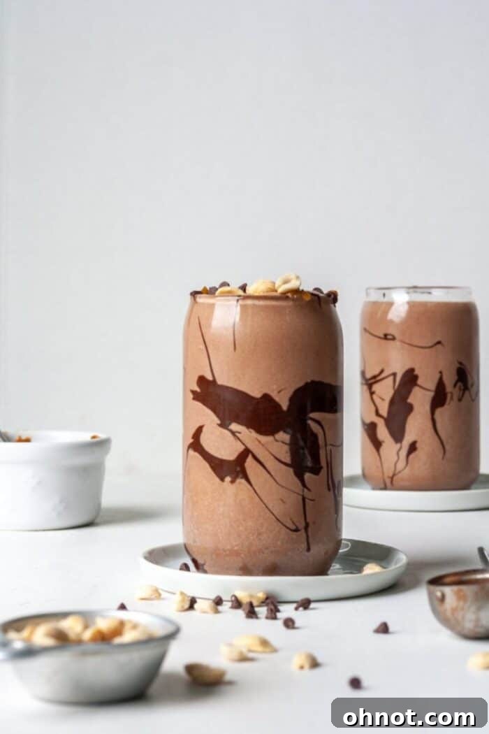 Healthy Snickers Smoothie in a glass, garnished with chopped peanuts and chocolate drizzle.