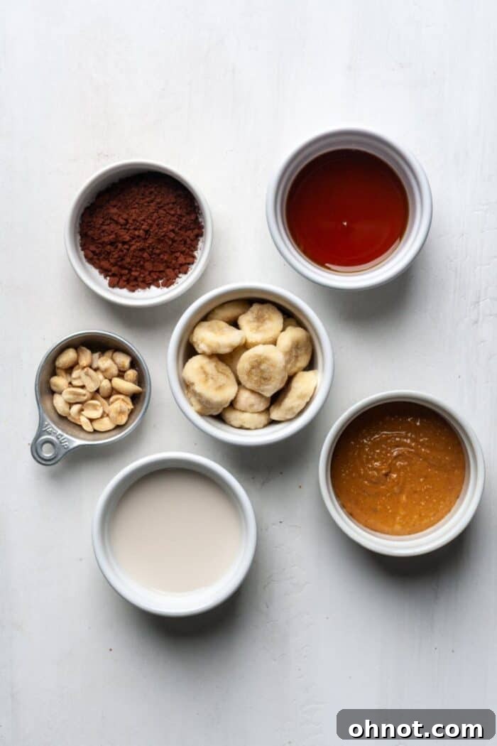 Collection of fresh ingredients for a healthy Snickers smoothie, including frozen banana, nuts, and cocoa powder.
