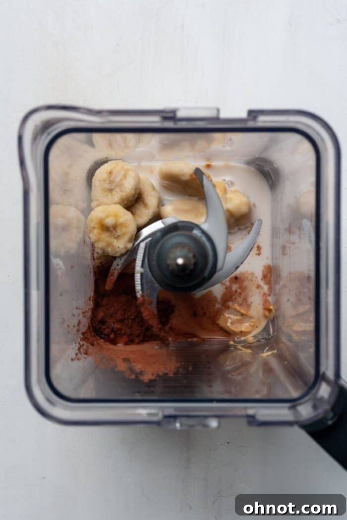 High-speed blender filled with ingredients for a Snickers smoothie, including frozen banana and cocoa powder.