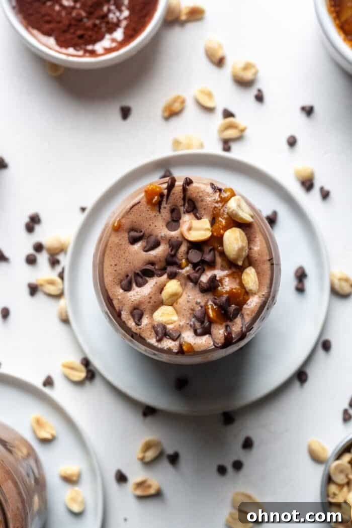 Healthy Snickers smoothie garnished with chopped peanuts and a rich chocolate drizzle, in a clear glass.