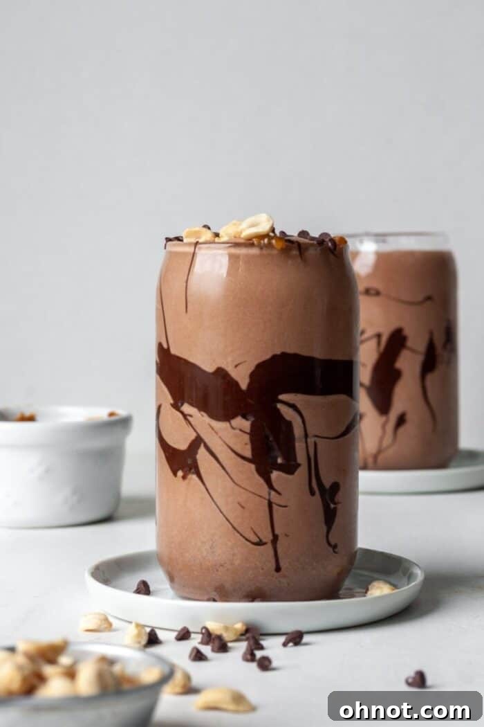 Close-up of a healthy Snickers smoothie in a glass, topped with peanut butter and chocolate drizzle, showing its rich texture.