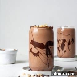Healthy Snickers Smoothie in a glass, garnished with chopped peanuts and chocolate drizzle.