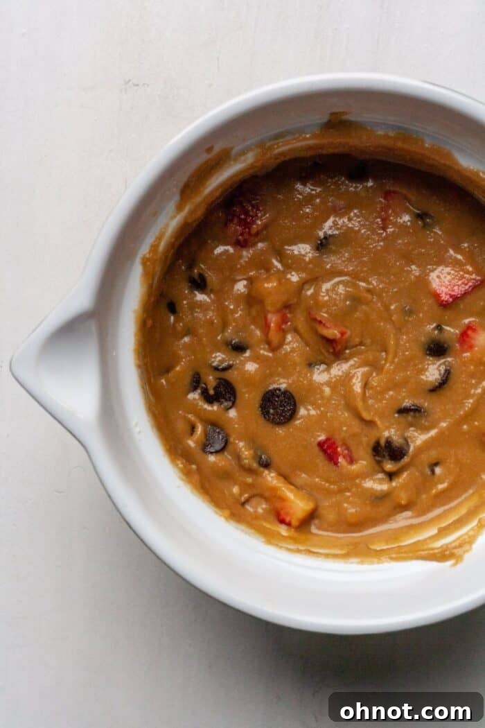 Gluten-free muffin batter with vibrant red strawberries and dark chocolate chips folded in.