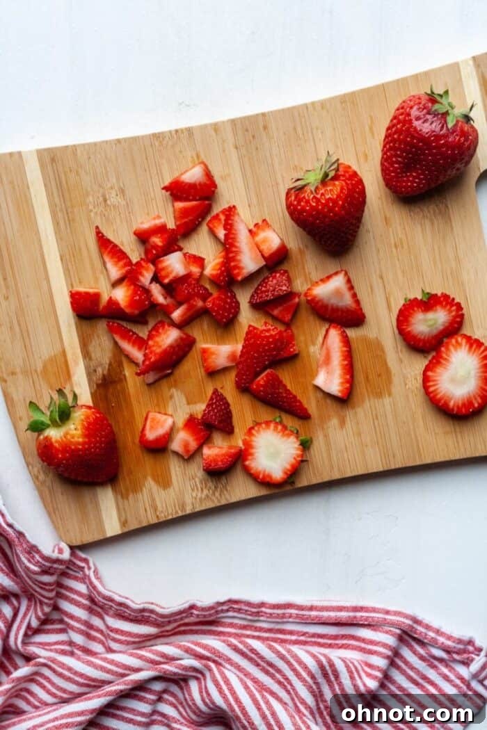 Fresh diced strawberries neatly arranged on a wooden cutting board.