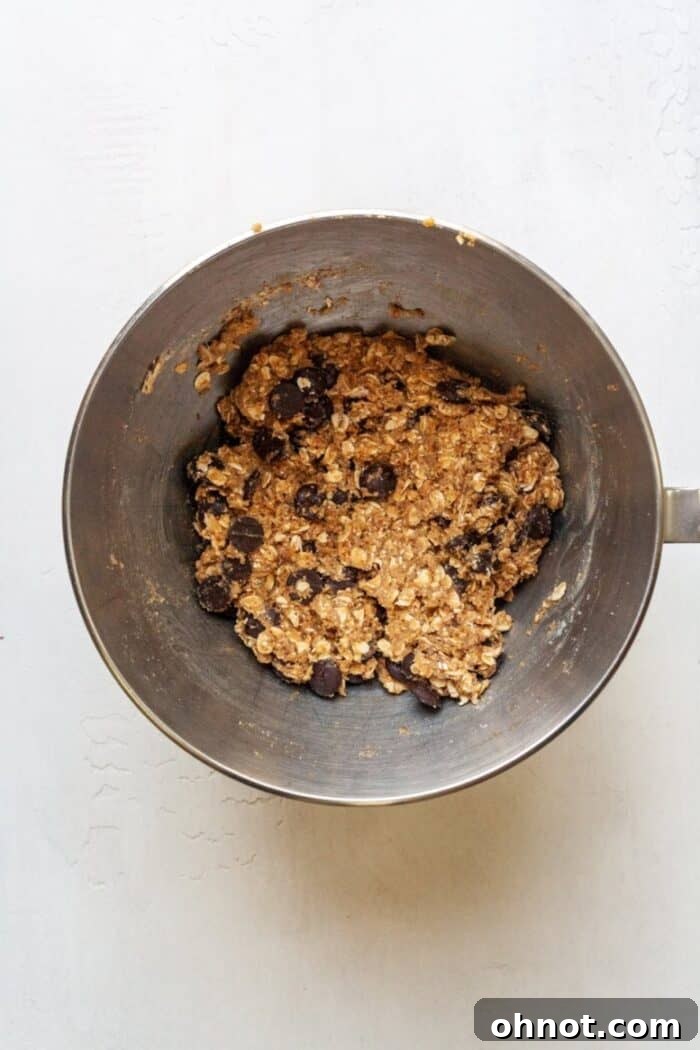 Almond flour, oats, and dark chocolate chips folded into the cookie dough in a mixing bowl.