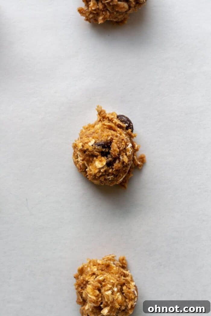 Uniform scoops of almond flour oatmeal cookie dough arranged on a parchment-lined baking sheet.