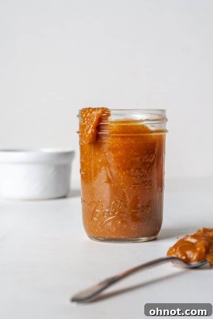 A spoon dipping into a jar of rich, vegan caramel sauce, highlighting its smooth and luscious consistency.
