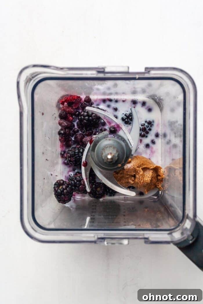 Frozen blueberries, blackberries, almond butter, and almond milk inside a blender cup, ready to be blended.