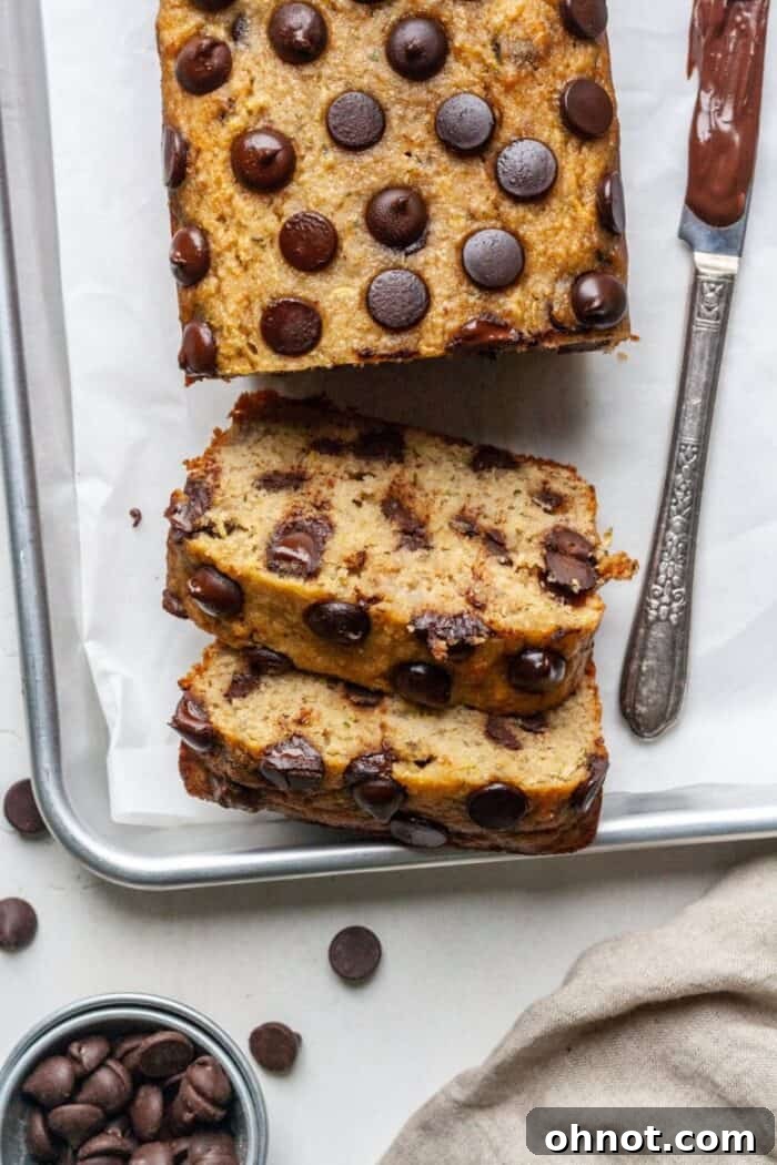 Freshly baked gluten-free zucchini banana bread cooling on a baking pan, topped with melted chocolate chips.