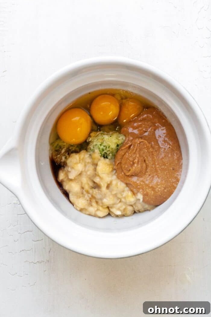 A large mixing bowl containing the wet ingredients for zucchini banana bread batter, including grated zucchini and mashed banana.