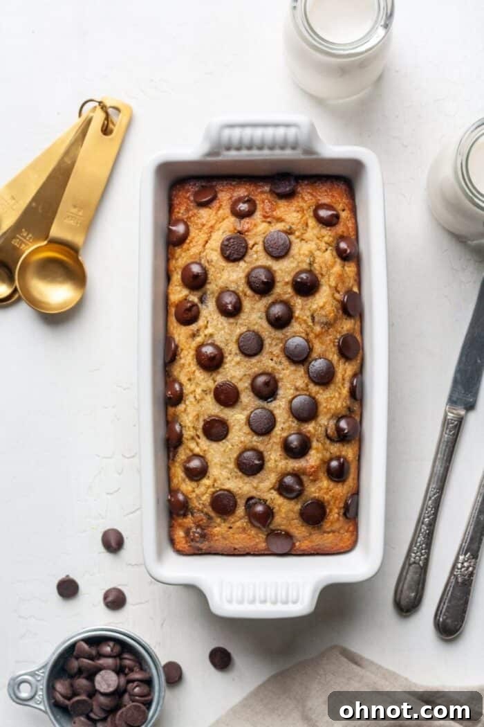 A golden-brown almond flour zucchini banana bread loaf in a white loaf pan, just out of the oven and cooling.
