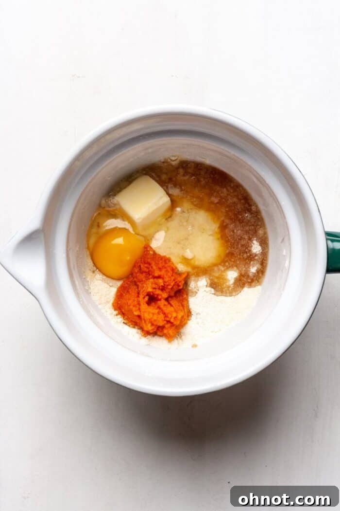 Wet ingredients including pumpkin puree added to a mixing bowl