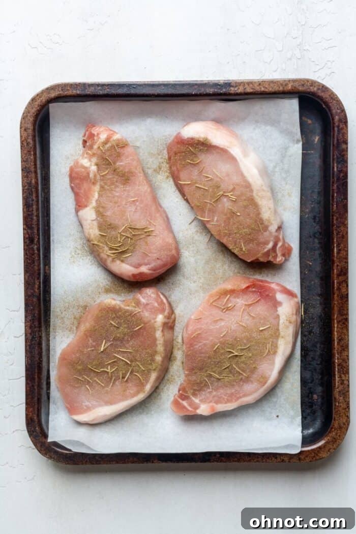 Raw pork chops seasoned with thyme, rosemary, and sea salt in a pan