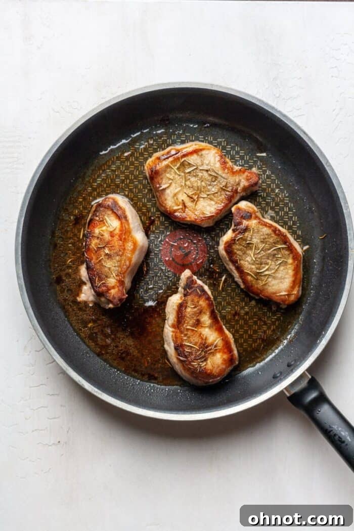 Pan with two perfectly seared AIP pork chops after flipping