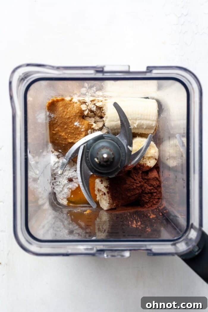 Blender filled with oats, banana, milk, and cocoa powder before blending