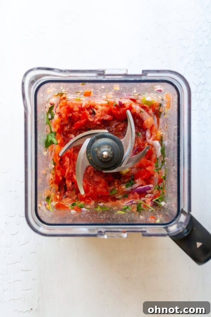 Partially blended salsa in a food processor, showcasing a desirable chunky texture, similar to pico de gallo, after a few pulses.