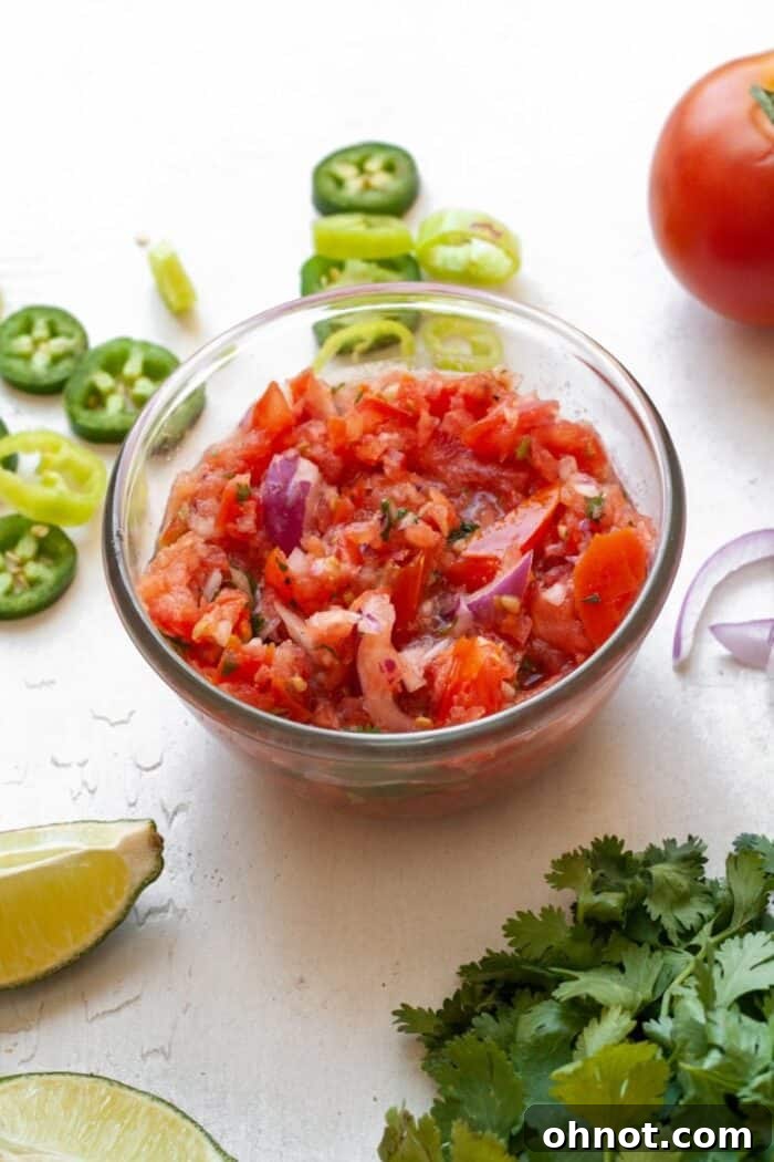 A beautifully presented glass bowl overflowing with fresh, chunky homemade Whole30 salsa, garnished with vibrant green cilantro sprigs, positioned on a light background and ready to be enjoyed.