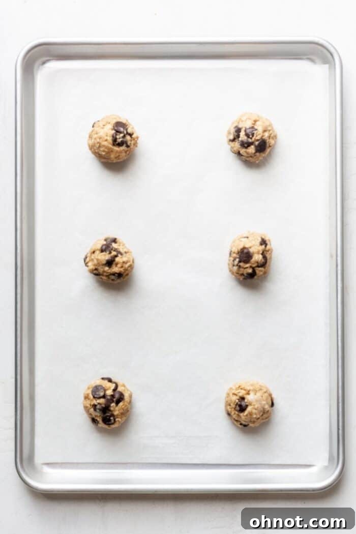 Scooped vegan oatmeal chocolate chip cookie dough balls on a parchment-lined baking sheet.