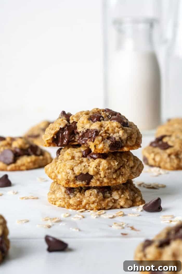 A stack of perfectly baked vegan oatmeal chocolate chip cookies, garnished with a few loose chocolate chips.