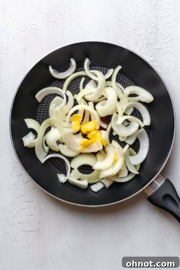 Sliced white onions cooking in butter in a large skillet over medium heat