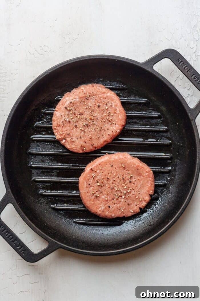 Raw turkey burgers seasoned and placed in a hot skillet with olive oil