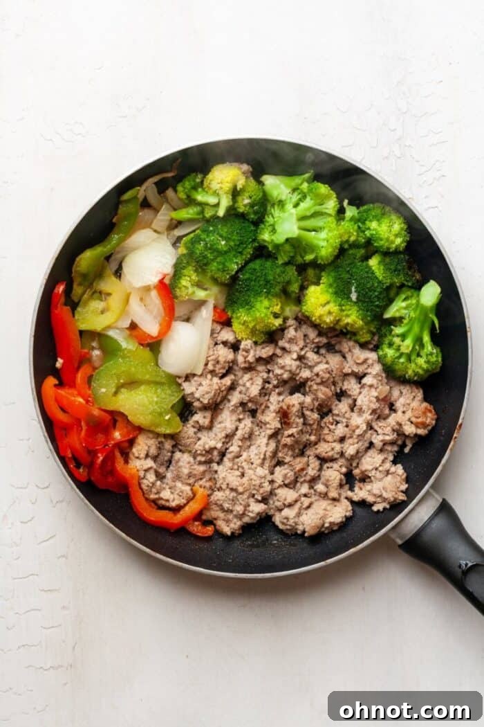 Ground turkey cooking with vegetables in a skillet, nearly browned.