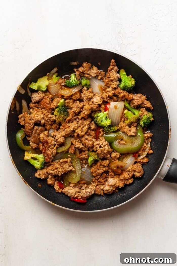 Teriyaki sauce being poured into a skillet with ground turkey and vegetables.