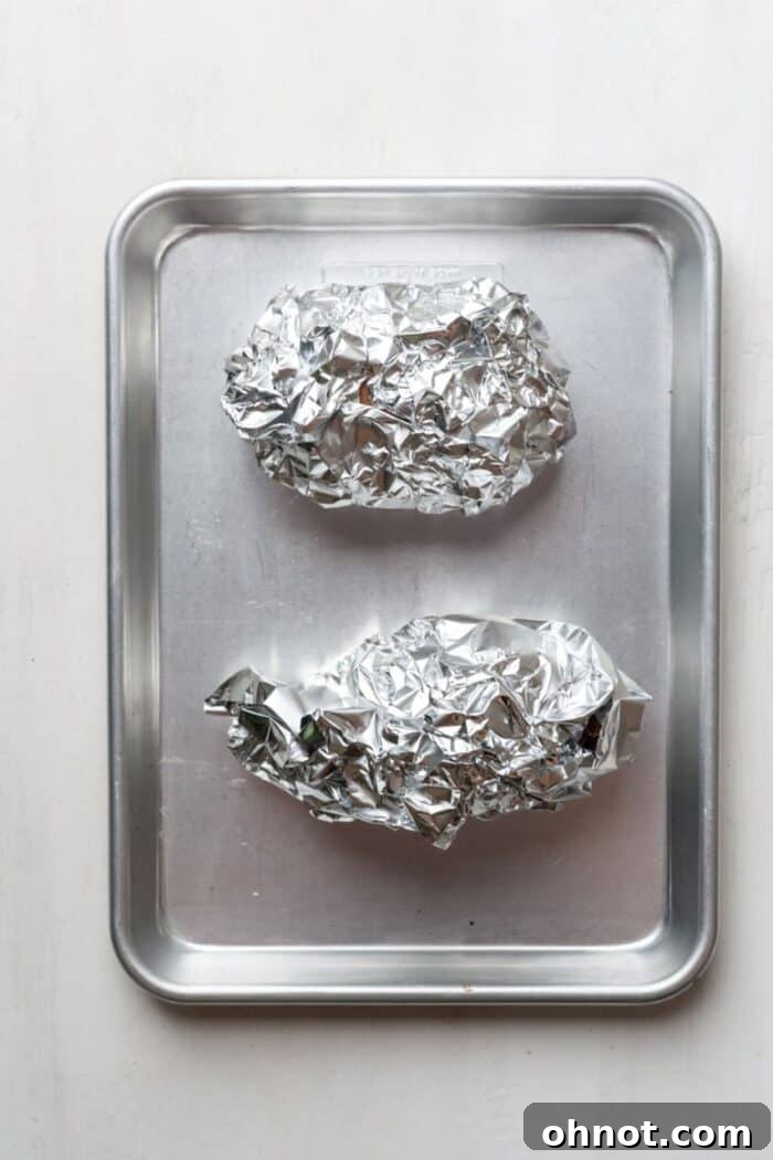 Sweet potatoes meticulously wrapped in tin foil, ready for roasting, resting on a baking sheet.