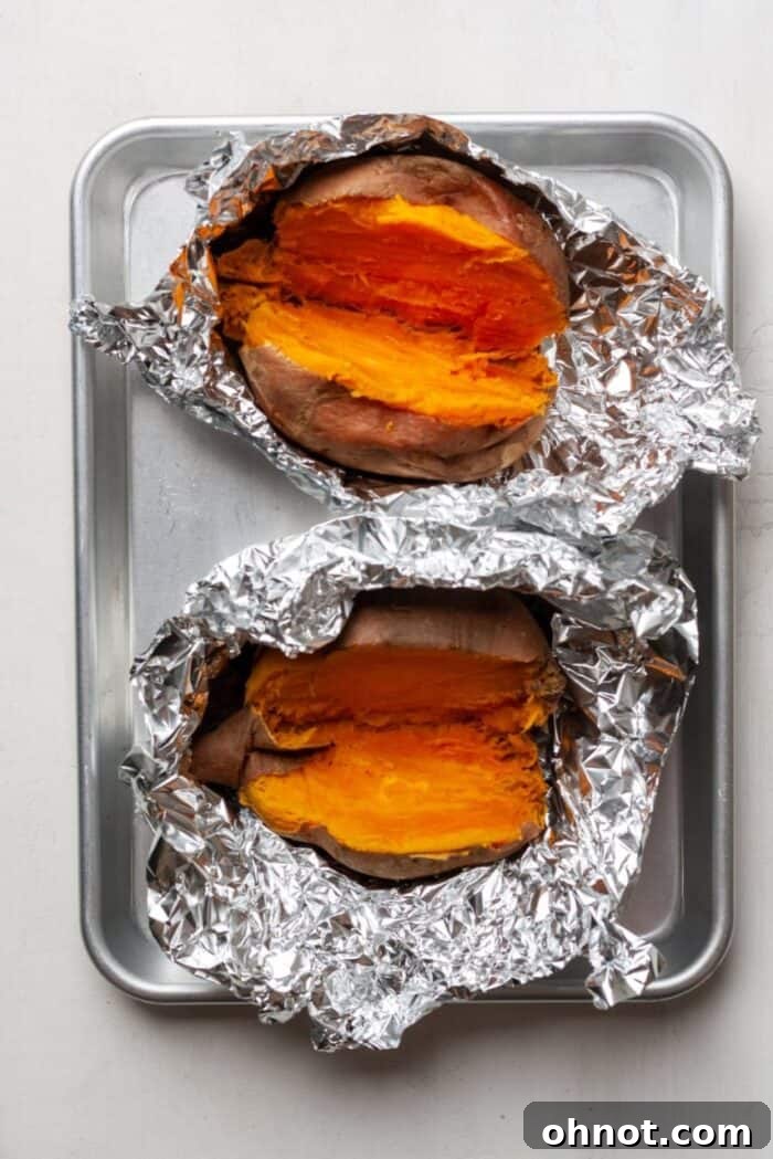 Freshly roasted sweet potatoes cooling on a baking pan after being removed from their foil wraps.