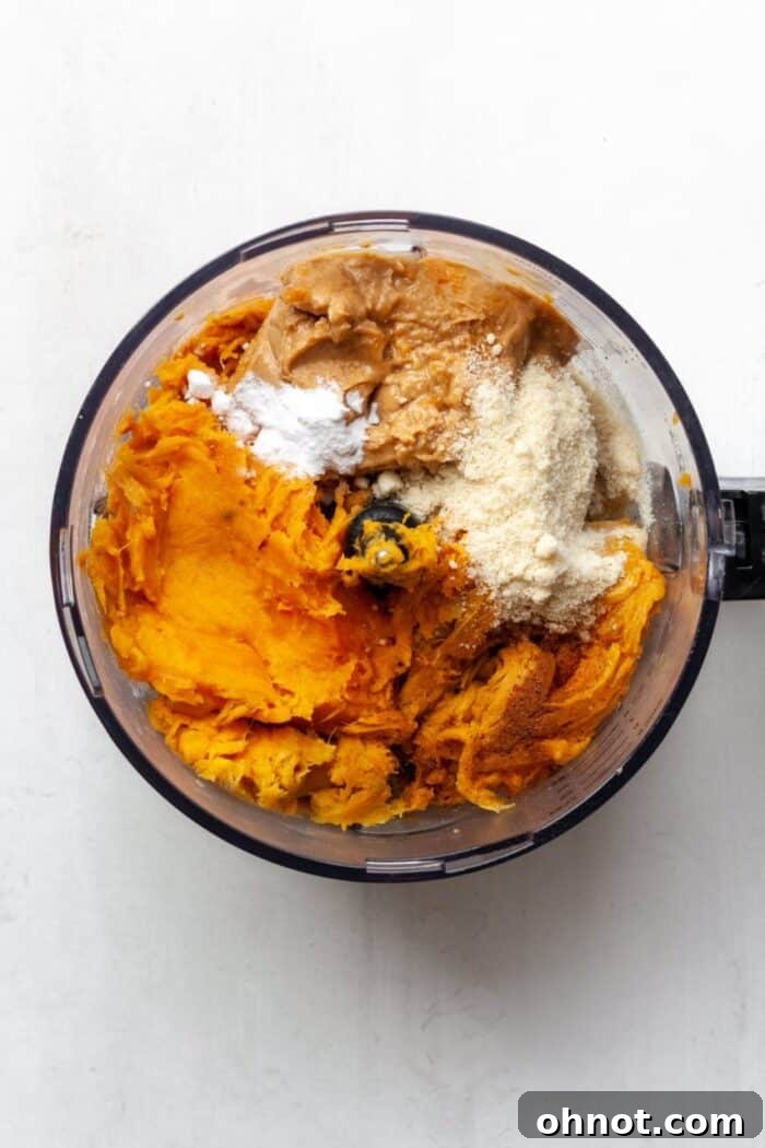 A food processor filled with scooped sweet potato flesh and other ingredients, ready for blending.