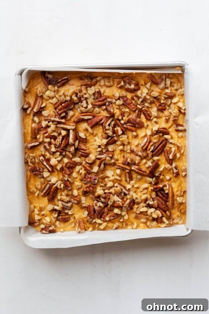 Sweet potato blondie batter evenly spread in a parchment-lined baking pan, topped with nuts, ready for the oven.